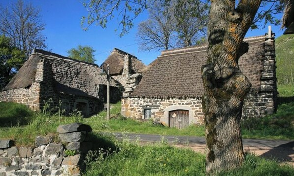 Un edificio de piedra con techo de paja, rodeado de follaje y árboles.