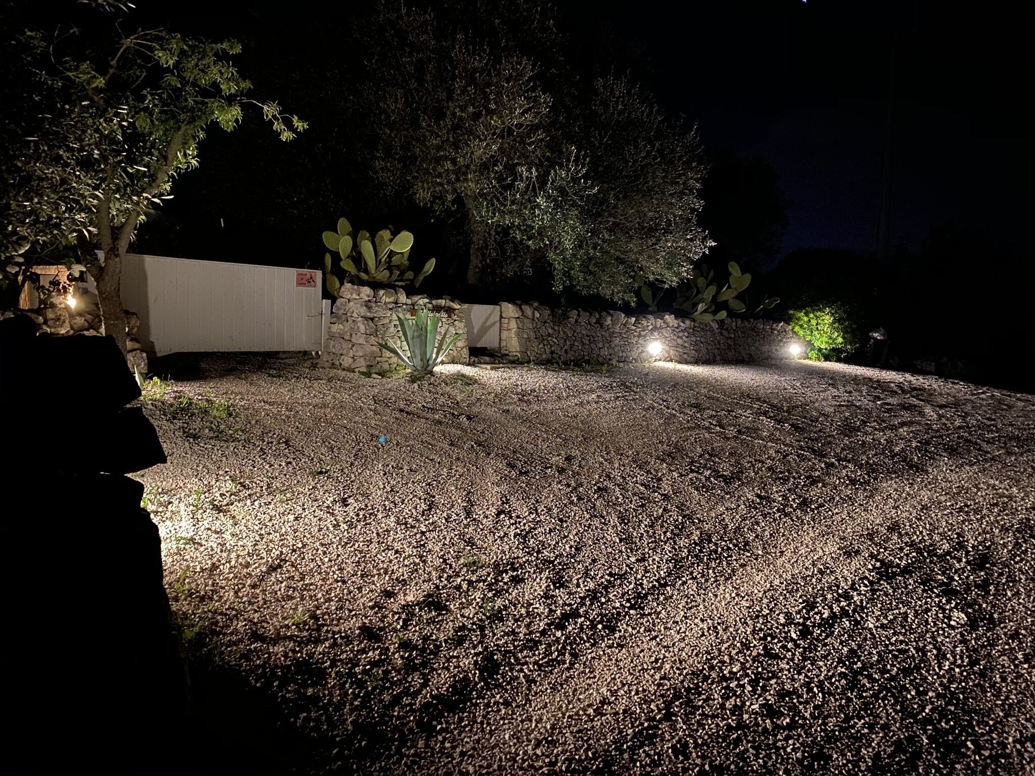 Ein Schotterweg bei Nacht mit einem weißen Gebäude und einer Steinmauer.