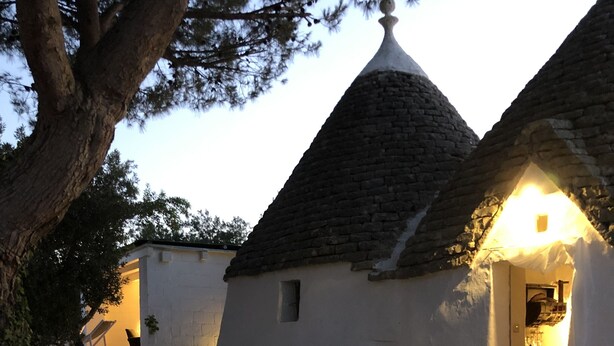 Una casa in pietra rustica con tetto in tegole, un vialetto in pietra che conduce all'ingresso e un piccolo giardino con piante in vaso.