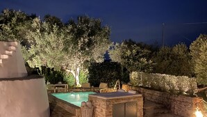 Una piscina in pietra circondata da un muro di pietra, con un albero e mobili da esterno.