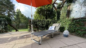 Une terrasse ensoleillée avec un fauteuil de relaxation, un grand parasol et une lanterne décorative.