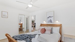 Un dormitorio con cama, mesitas de noche, ventilador de techo y puerta que da a un baño.