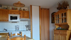 A kitchen with wooden cabinets, a microwave, and a dining area with a table and chairs. - 2-room cabin apartment, up to 6 people, pets allowed in Bolquère (Bolquère-Pyrénées 2000)