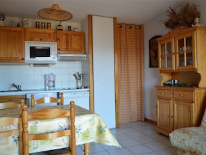 A kitchen with wooden cabinets, a microwave, and a dining area with a table and chairs. - 2-room cabin apartment, up to 6 people, pets allowed in Bolquère (Bolquère-Pyrénées 2000)