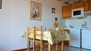 A dining area with a table covered by a tablecloth, wooden chairs, a kitchen with a microwave and a dishwasher, and a wall-mounted picture. - 2-room cabin apartment, up to 6 people, pets allowed in Bolquère (Bolquère-Pyrénées 2000)