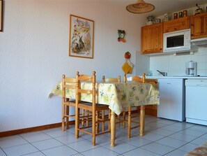 A dining area with a table covered by a tablecloth, wooden chairs, a kitchen with a microwave and a dishwasher, and a wall-mounted picture. - 2-room cabin apartment, up to 6 people, pets allowed in Bolquère (Bolquère-Pyrénées 2000)