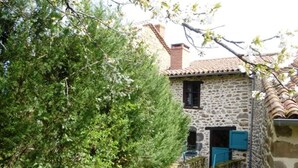 Un edificio in pietra con una piccola finestra e un portone, immerso nel verde.