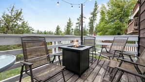 Une terrasse extérieure dotée d’un foyer, de sièges et offrant une vue sur des arbres et un bâtiment.