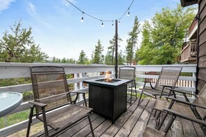 Una terrazza esterna con un elemento decorativo a fuoco, posti a sedere e vista su alberi e un edificio.