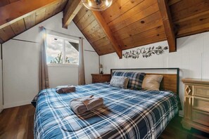 Una camera da letto con soffitto in legno, un letto con copripiumino a quadri, un comodino e una cassettiera.
