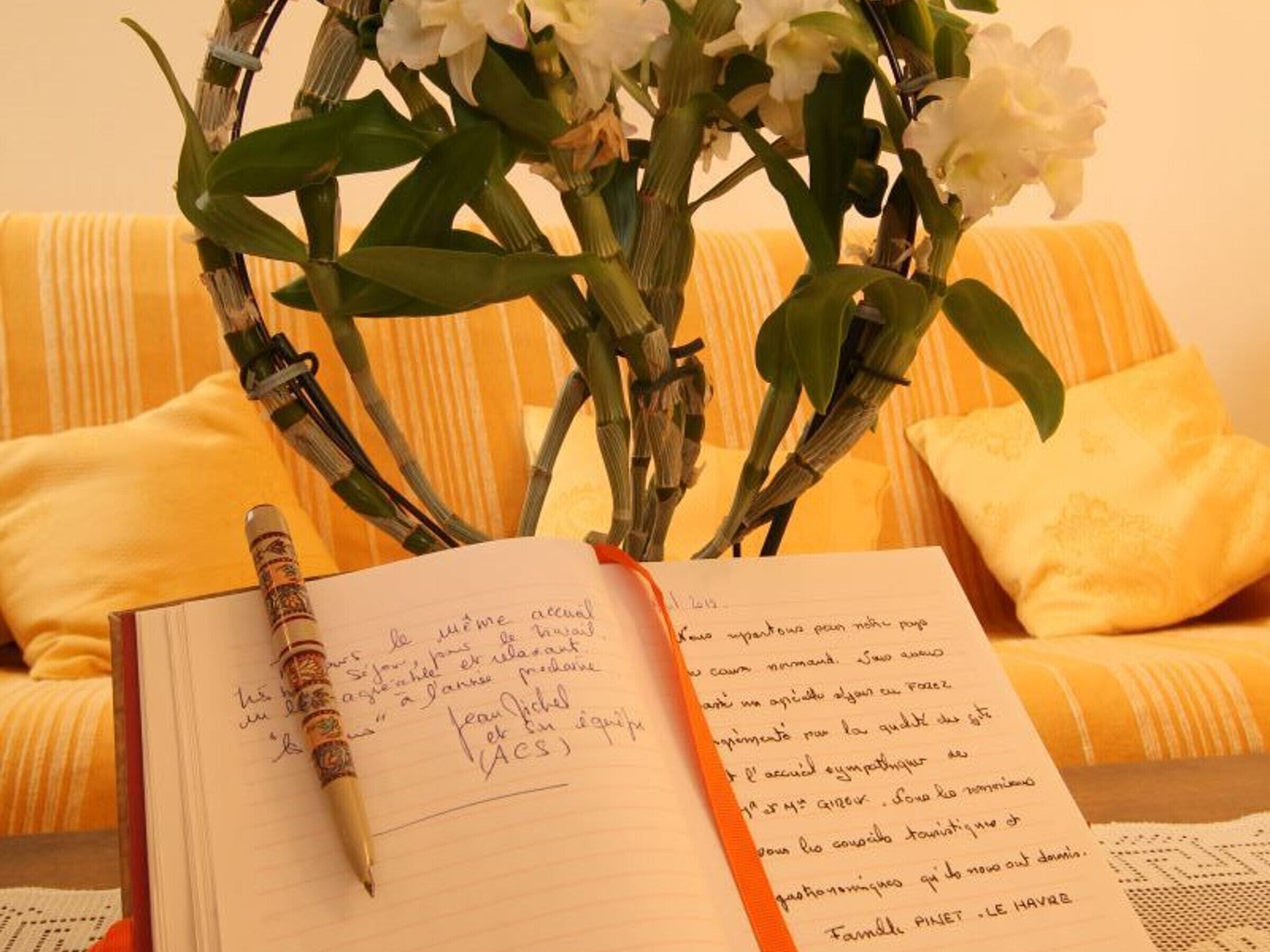 A notebook with handwritten notes, a pen, and a bouquet of white flowers on a yellow striped sofa.