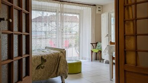 Ein Schlafzimmer mit einem Bett, einem grünen Hocker, einem Sessel und einem Tisch mit einer Lampe.