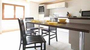 Uma cozinha moderna com uma ilha central, armários brancos e uma área de jantar com cadeiras pretas.