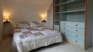 Quarto com cama, duas luminárias de cabeceira, um guarda-roupa espaçoso com várias gavetas e teto inclinado.