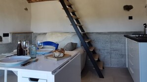Una cocina con techo de madera, pared de concreto y escalera de madera. Hay una mesa con un plato, un vaso y una botella.