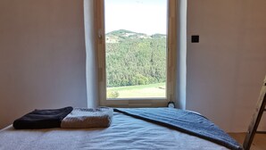 Un dormitorio con cama, ventana y vista a zona boscosa.