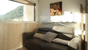 A modern living room with a large window, a sofa, and a painting on the wall.