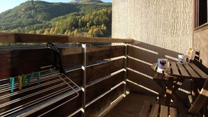 A balcony with a view of a mountain, a wooden table with a mug, and a clothes drying rack.