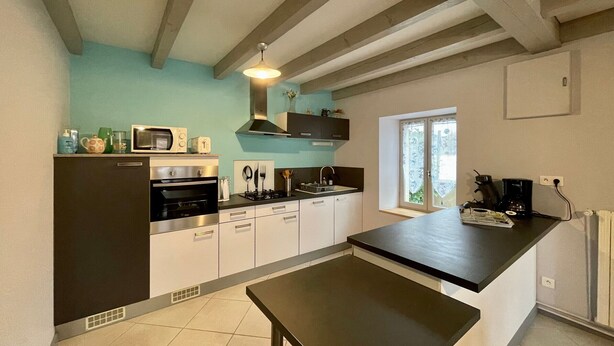 A modern kitchen with a central island, built-in oven, microwave, and gas stove. There is a window with a view of greenery outside.