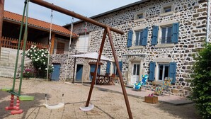 A stone building with blue shutters, a swing set, and outdoor seating.