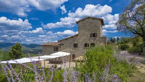Um edifício de pedra com terraço e área de estar ao ar livre, rodeado por vegetação e lavanda.