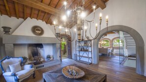 Uma sala de estar acolhedora com lareira, um candelabro e uma mesa de madeira.