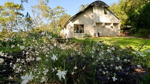 Une maison avec un toit en pente, entourée d’une pelouse bien entretenue et de plantes en fleurs.