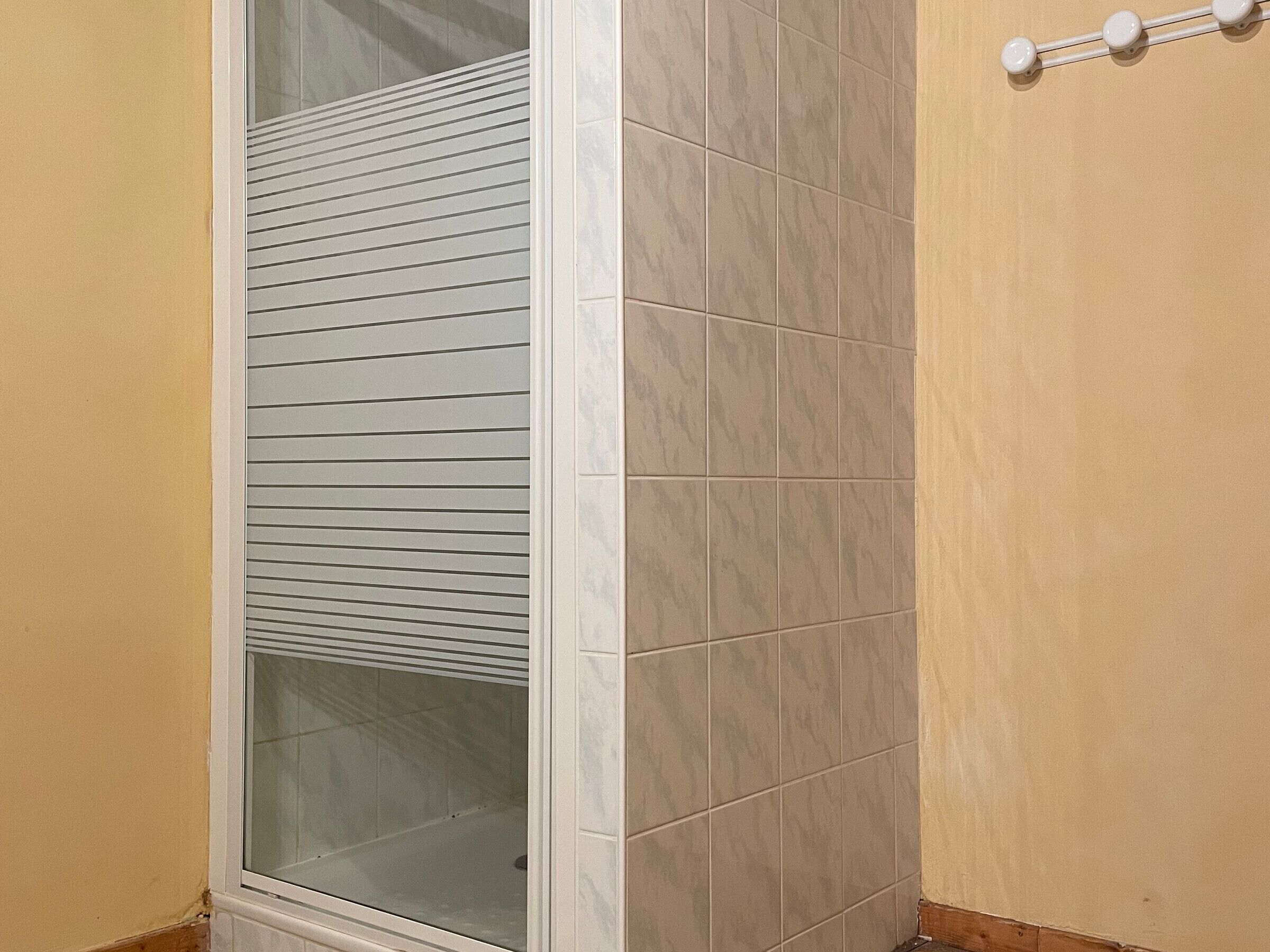 A corner of a room with beige walls, a tiled floor, and a window with horizontal blinds.