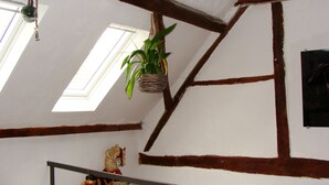 A room with exposed wooden beams, a hanging plant, a small horse figurine, and a window with natural light. - Cottage Hühnerstall (Zülpich)