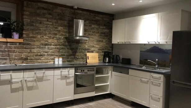 A modern kitchen with white cabinets, a stainless steel range hood, a built-in oven, and a large window with a mountain view. - Cottage Hühnerstall (Zülpich)