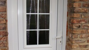 A white door with a glass panel and a small window, set against a brick wall. - Cottage Hühnerstall (Zülpich)