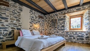 A stone-walled bedroom with a wooden bed, a nightstand, and a window. - Luxury Gîte with Spa, Terrace, and Game Room in Scenic Blanlhac, Rosières (Rosières)