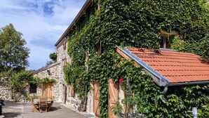 A stone building with a red-tiled roof, wooden shutters, and a gravel courtyard. - Luxury Gîte with Spa, Terrace, and Game Room in Scenic Blanlhac, Rosières (Rosières)