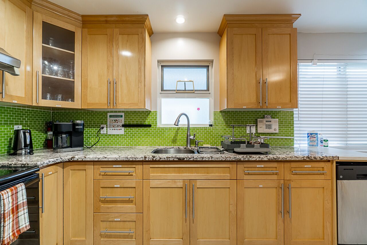 A kitchen with wooden cabinets, a granite countertop, a coffee maker, and a window above the sink.