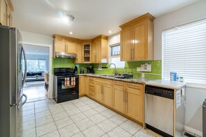 Een moderne keuken met houten kastjes, een roestvrijstalen koelkast, een vaatwasser en een groene tegelachterwand.