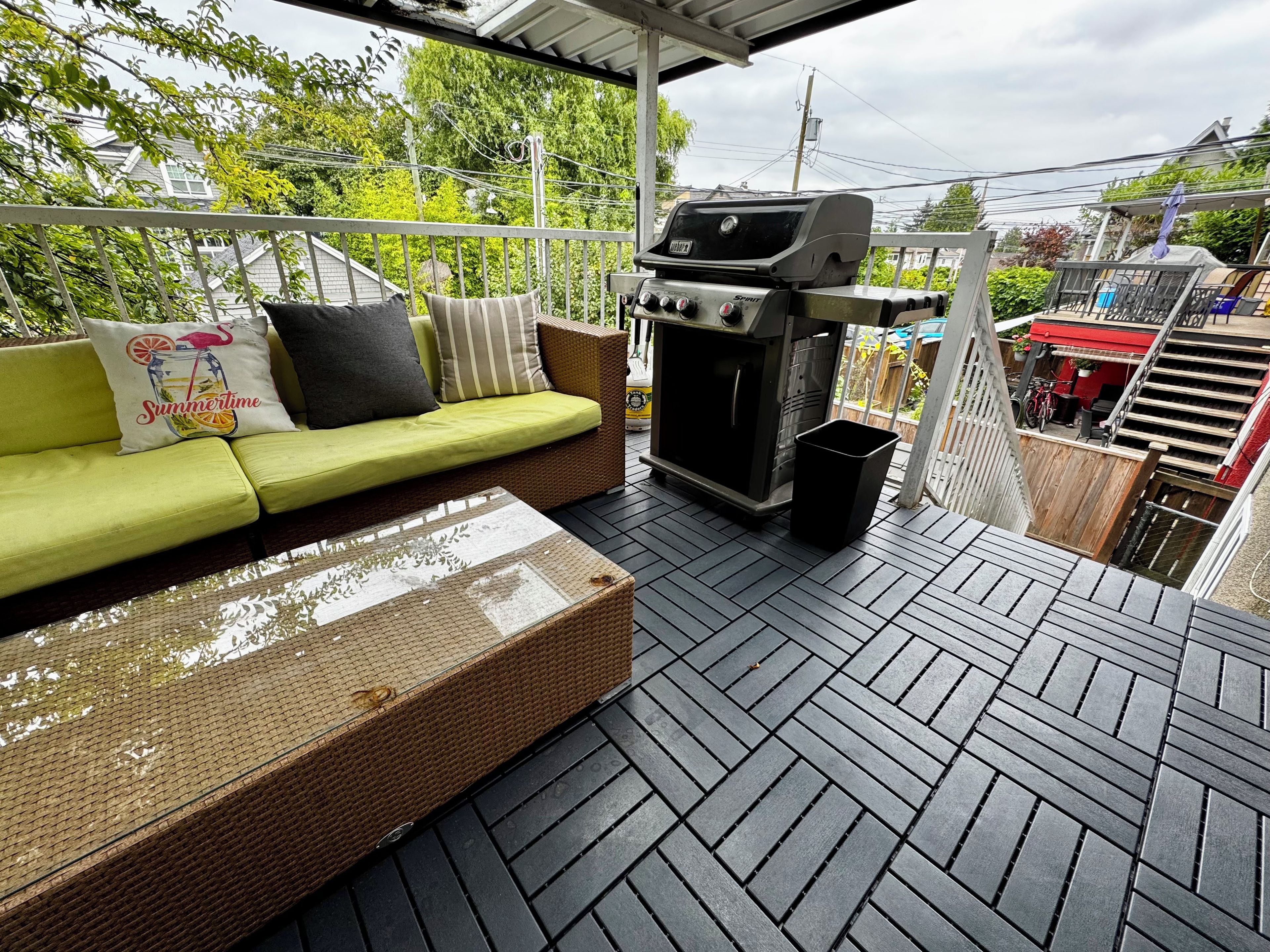 An outdoor patio with a green sofa, a grill, and a trash bin.