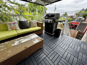 Un patio exterior con un sofá verde, una parrilla y un basurero.