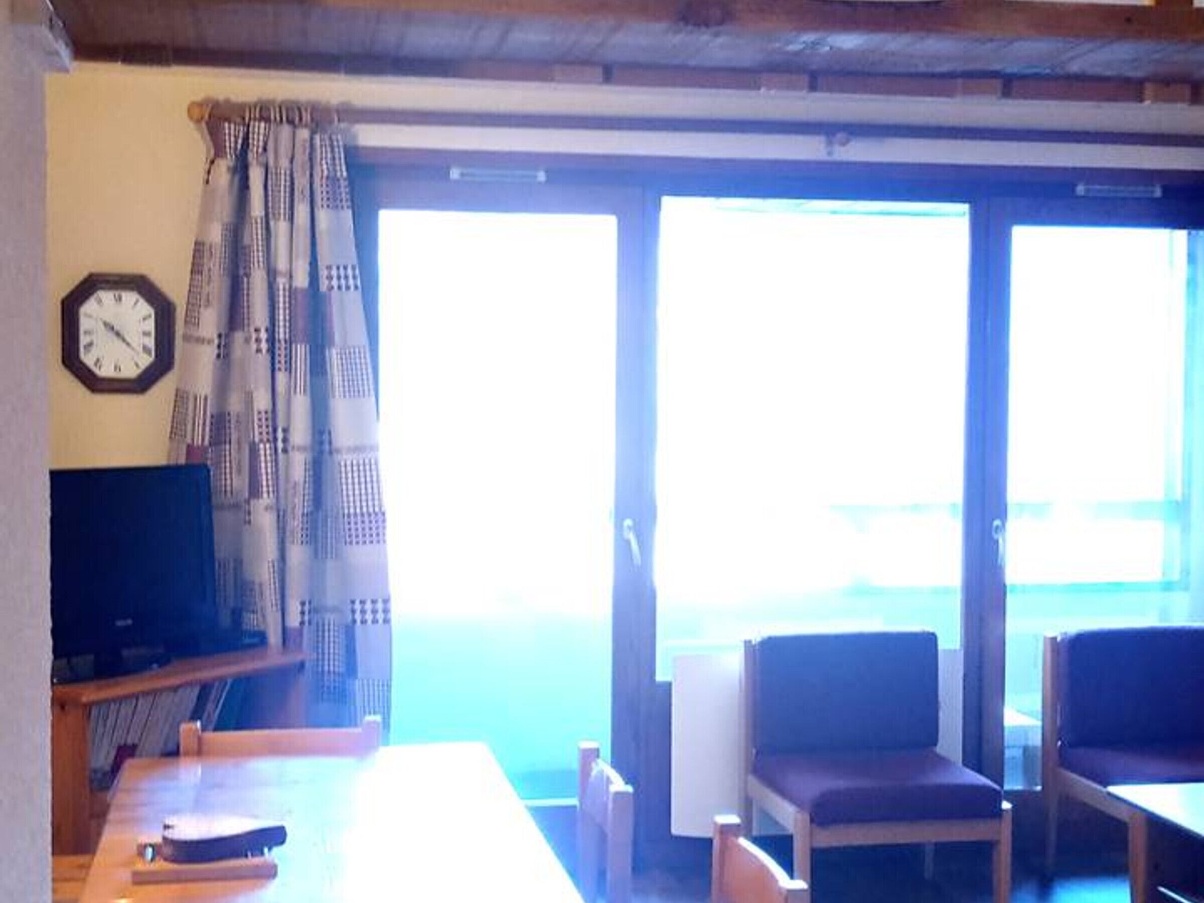 A room with a wooden table, two chairs, a television, and a window with curtains.