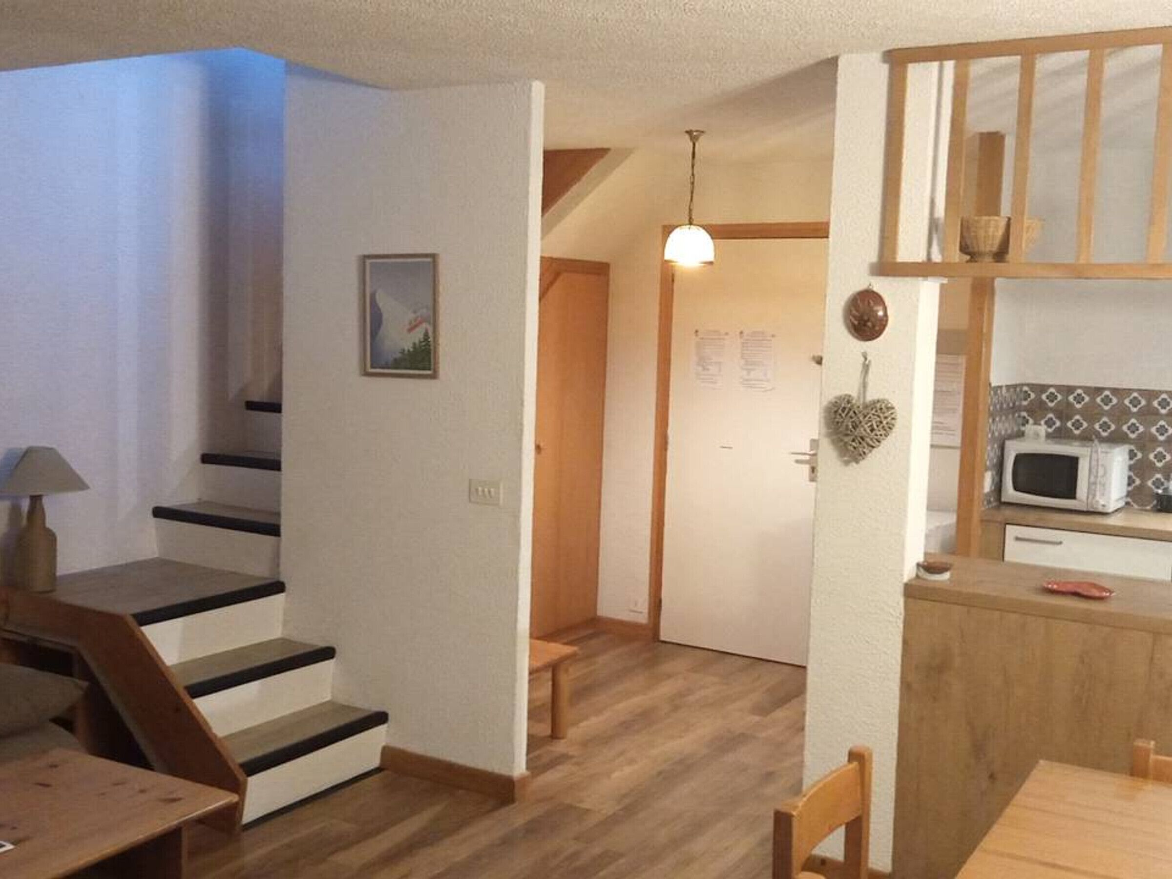 Un escalier menant à une porte, un coin repas avec une table et des chaises, et un espace cuisine équipé d’un four à micro-ondes.