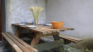 Une table de pique-nique en bois avec des bancs, un vase contenant des plantes séchées et un panier en osier.