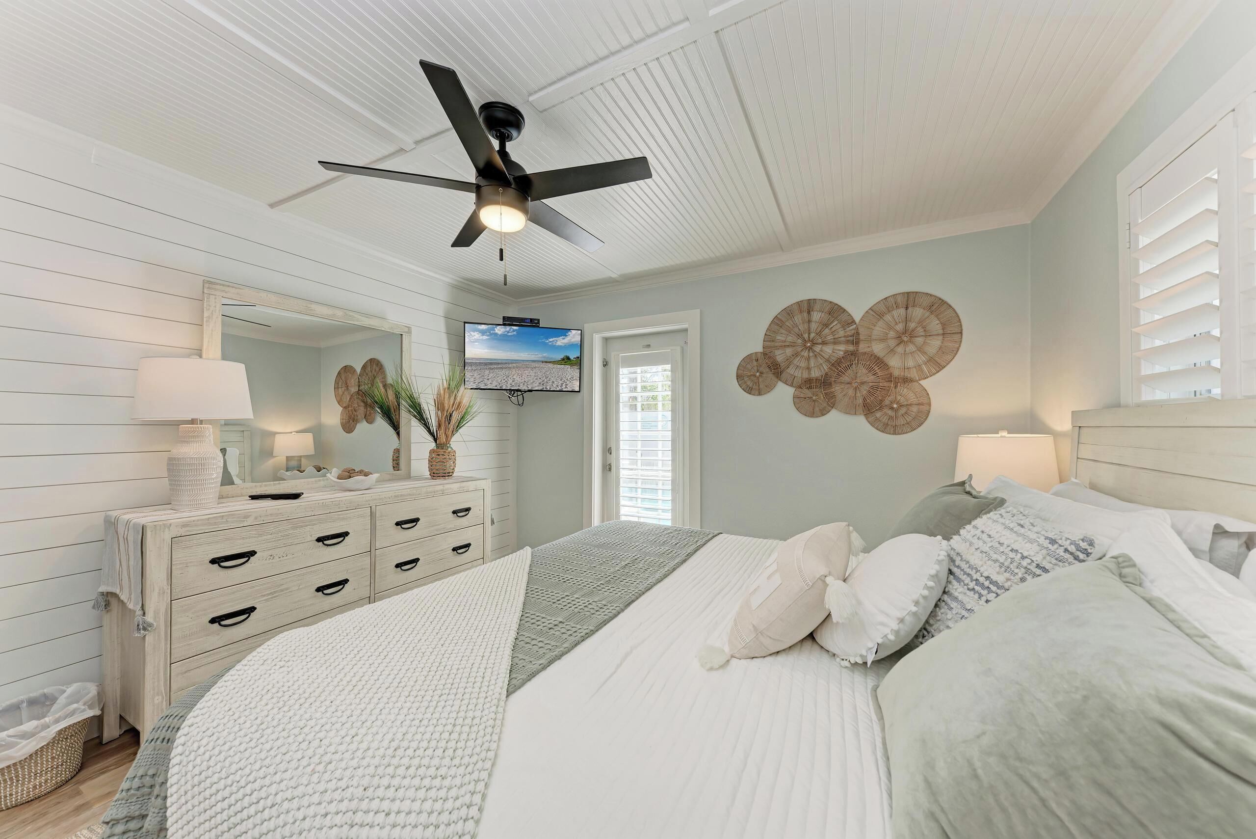 Une chambre à coucher avec un lit, un ventilateur de plafond, une télévision et une commode.