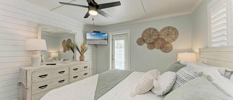 Une chambre à coucher avec un lit, un ventilateur de plafond, une télévision et une commode.