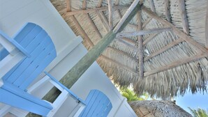 A beachside hotel room with a thatched roof, blue doors, and a wooden floor.