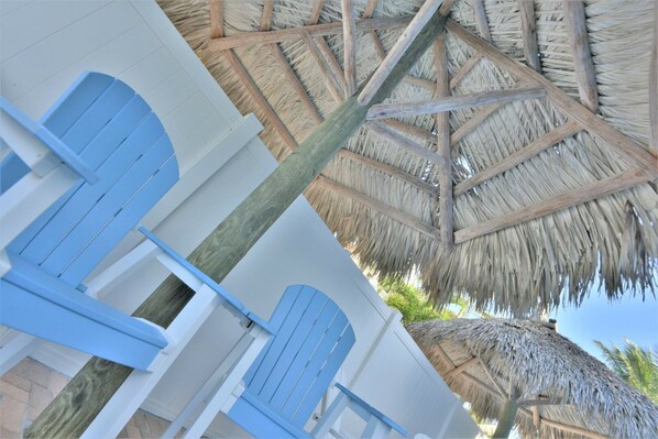 A beachside hotel room with a thatched roof, blue doors, and a wooden floor.