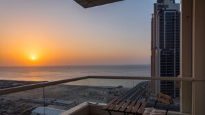Ein Balkon mit Blick auf den Sonnenuntergang über dem Meer, ein Hochhaus und ein Parkplatz.