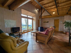 A cozy cabin interior with a wooden ceiling, a large window, a television, a sofa, and a fireplace.