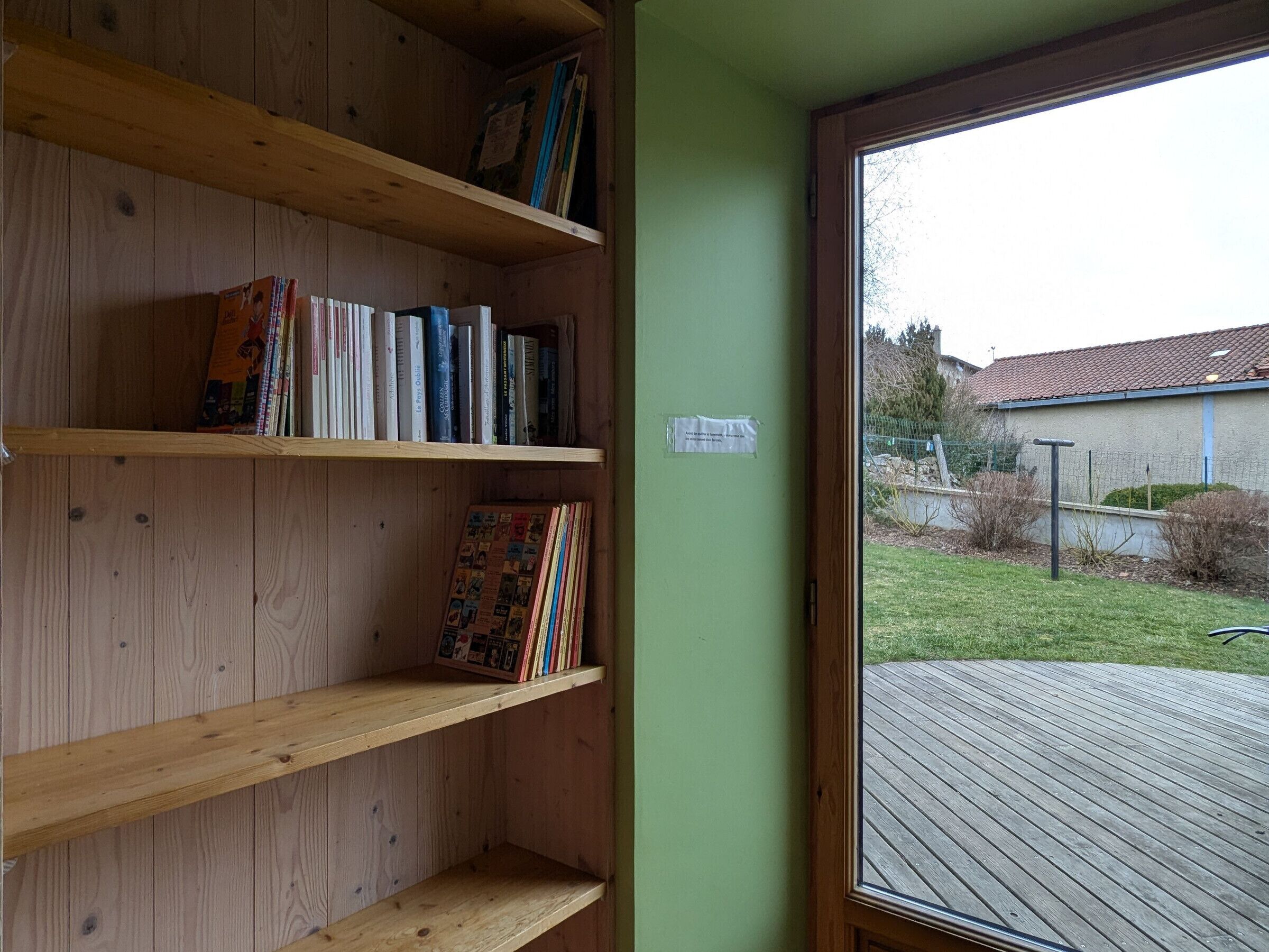 Una habitación con una estantería de madera, una pared verde y vistas a un patio trasero a través de una puerta de vidrio.