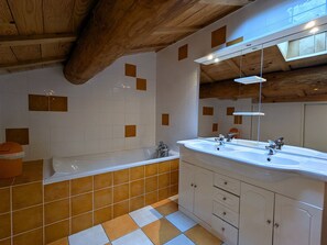 Ein Badezimmer mit Holzbalkendecke, weißen und braunen Fliesen, einer Badewanne, einem Waschbecken mit Spiegel und Schränken.