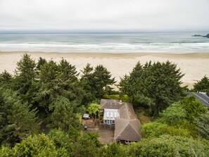 Une propriété située sur la côte, avec une maison entourée d’une forêt dense, offrant une vue sur une plage de sable et l’océan.