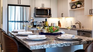 Une cuisine moderne avec des meubles blancs, un réfrigérateur en acier inoxydable, un four à micro-ondes et un coin repas agrémenté d’assiettes, de verres et d’une salade.